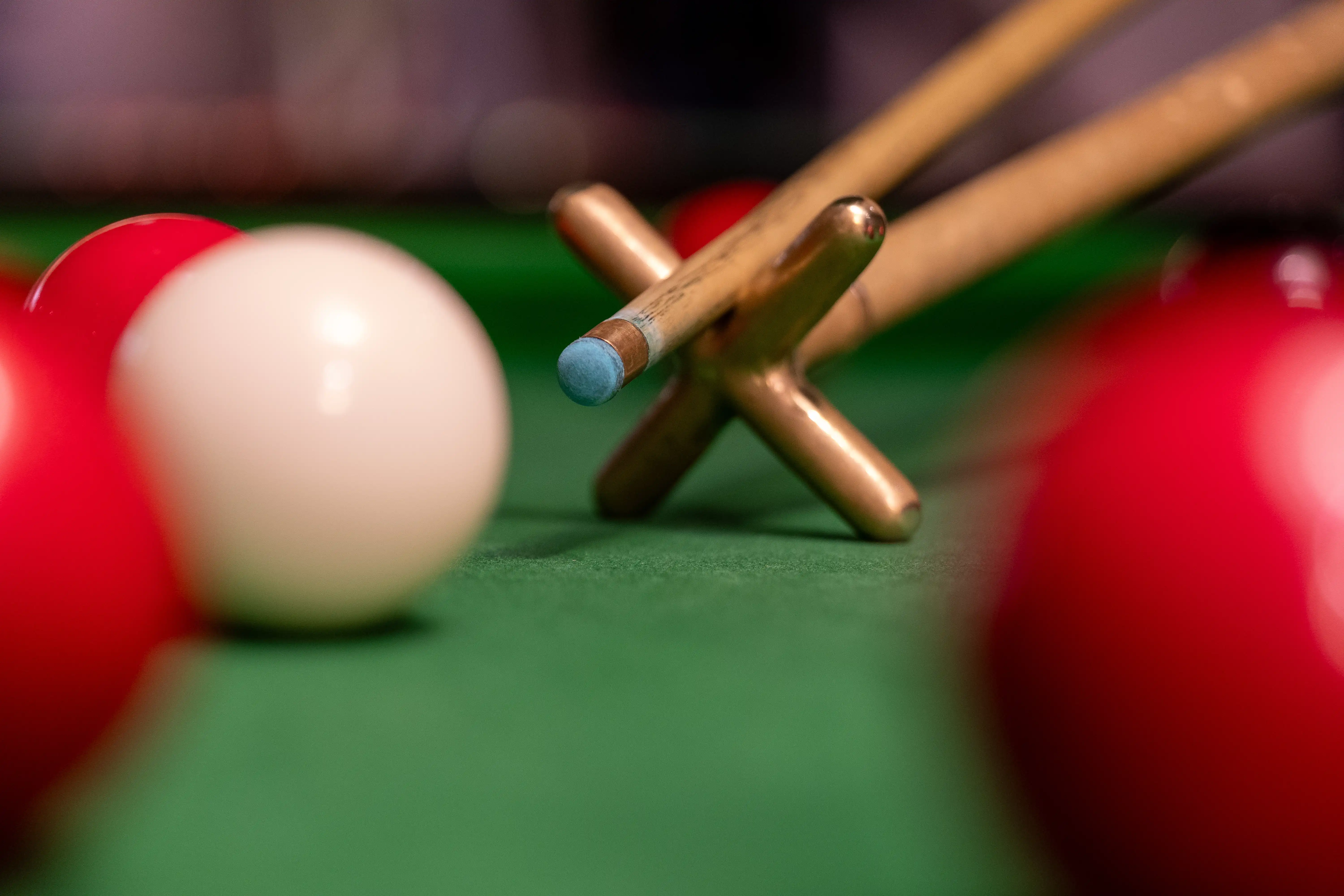 Voorkant van de snooker stok die de witte bal richting de rode ballen slaat ingezoomed.